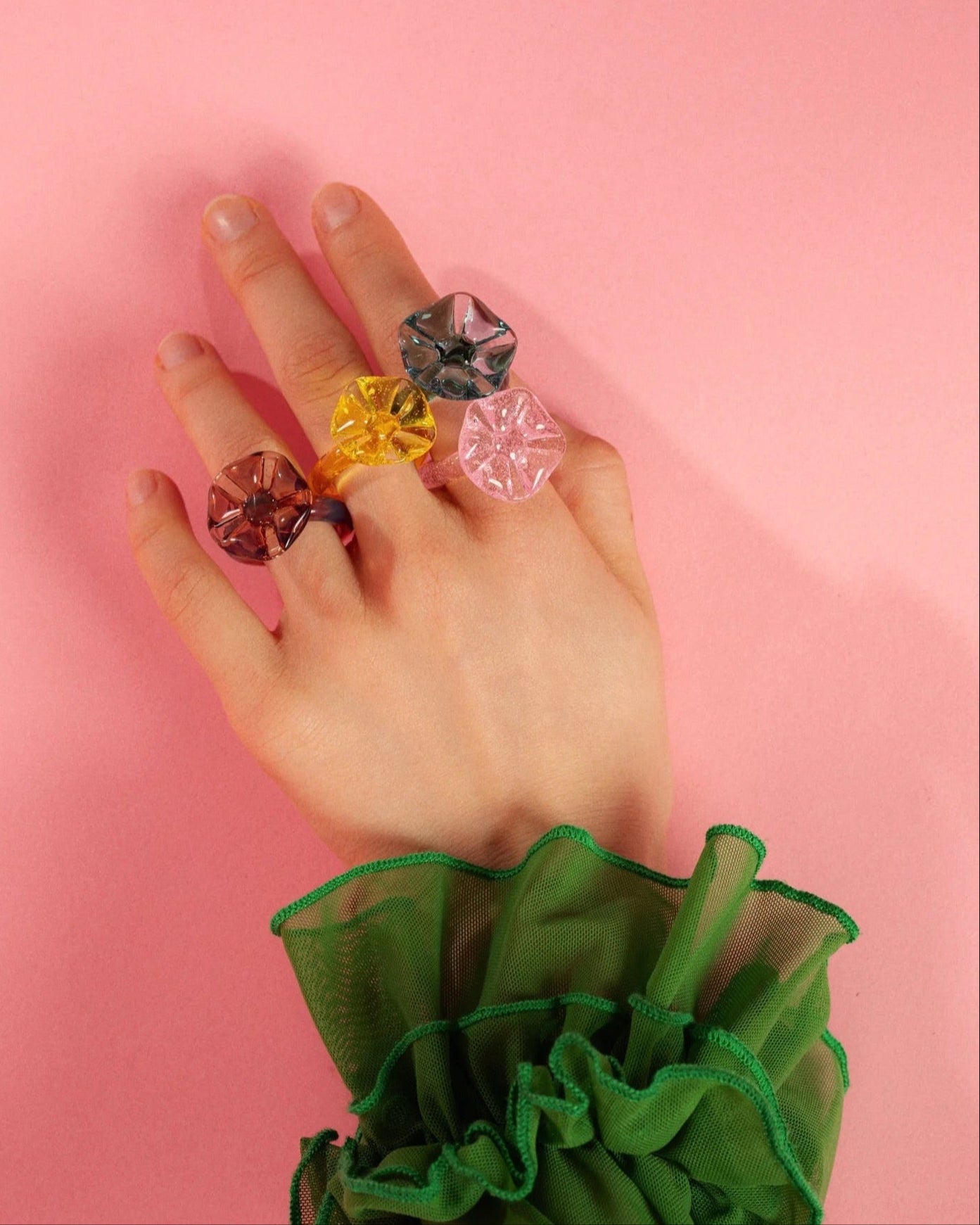 Hand wearing colorful rings on a pink background