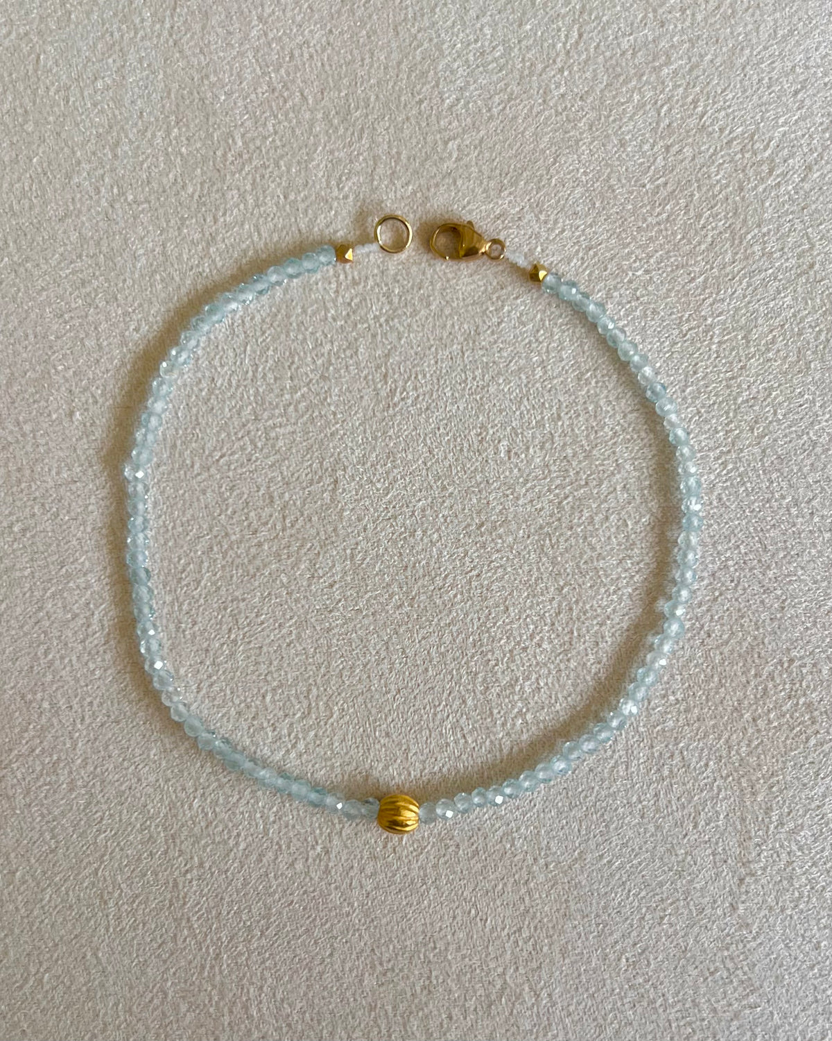 Margaret Solow designer, A faceted blue topaz beaded bracelet with a 18k yellow gold round bead in the center and a 14k clasp, displayed against a light background.
