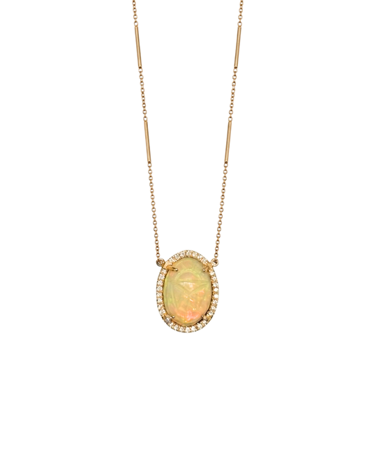 A gold necklace featuring an oval opal pendant with a halo of small clear stones, displayed against a solid white background.