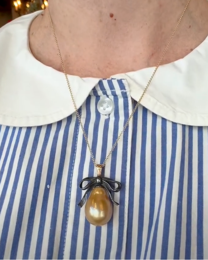 Necklace with a large pendant worn by a person in a blue and white striped shirt.